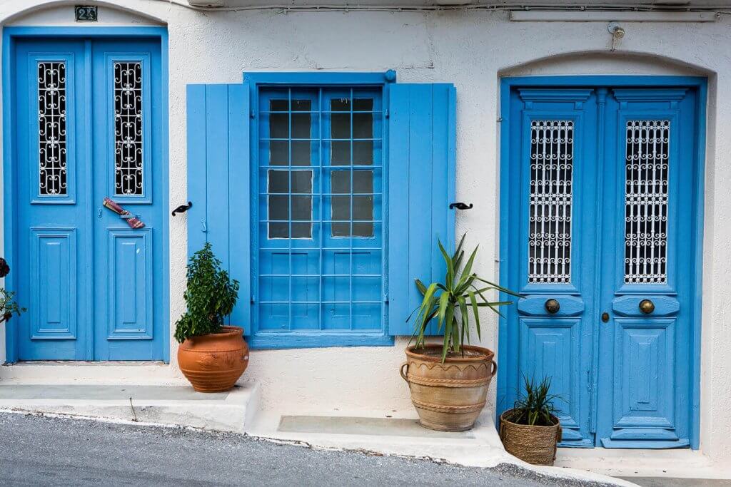 A blue painted door and window of a small white house in Crete.