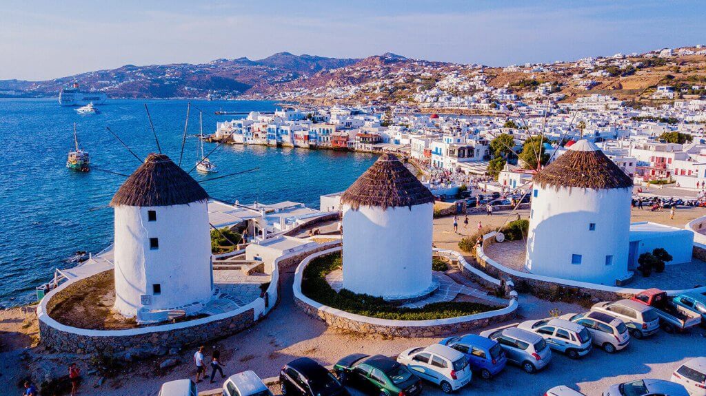 Three white towers of Mykonos City with the sea next to them.