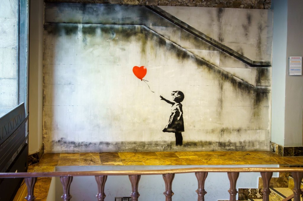 A black and white art painting by Banksy with a girl holding a red balloon.