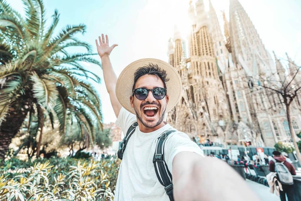 A young man smiling and making a selfie infront of the Sagrada Familia.