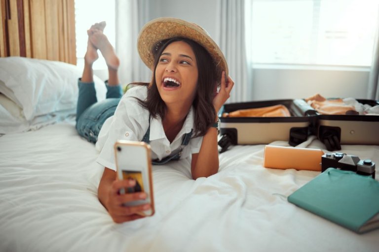 A happy woman in a hotelroom lying on the bed and taking a selfie.