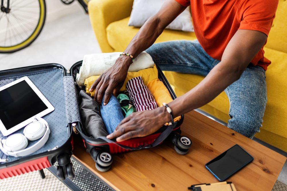 A man rolling his clothes to fit better in the suitcase.