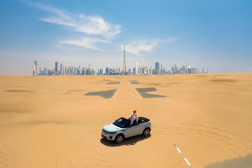 A 4x4 in the desert with the skyline of Dubai in the background.