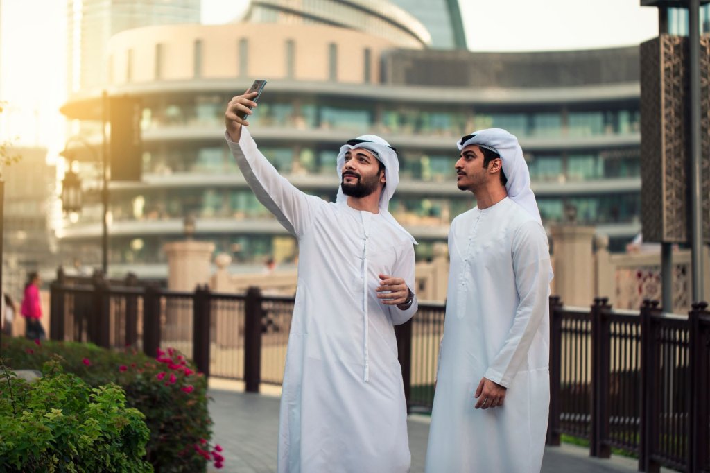 Two arabic man with tradiotional clothes are taking a selfie.