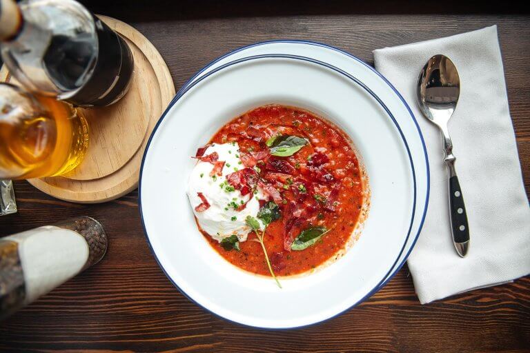 White plate with tomato soup and a scoop of ricotta