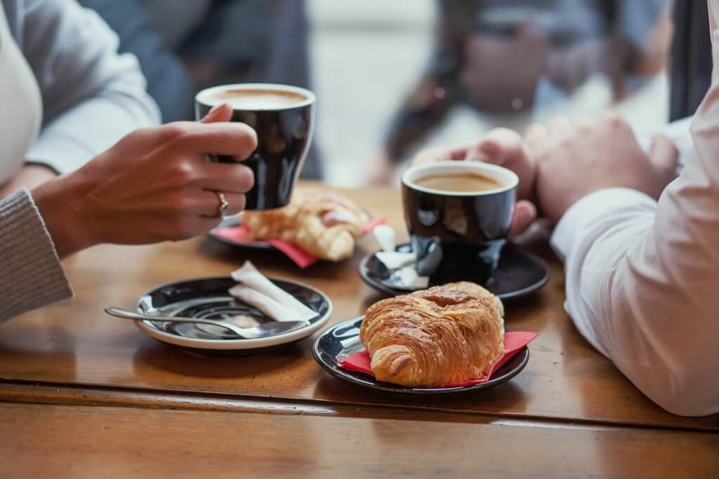 Two persons drinking a coffee ad having a croissant.