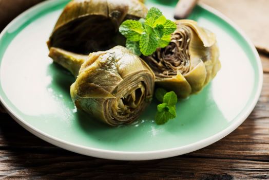 Three cooked artichokes served on a mint green plate