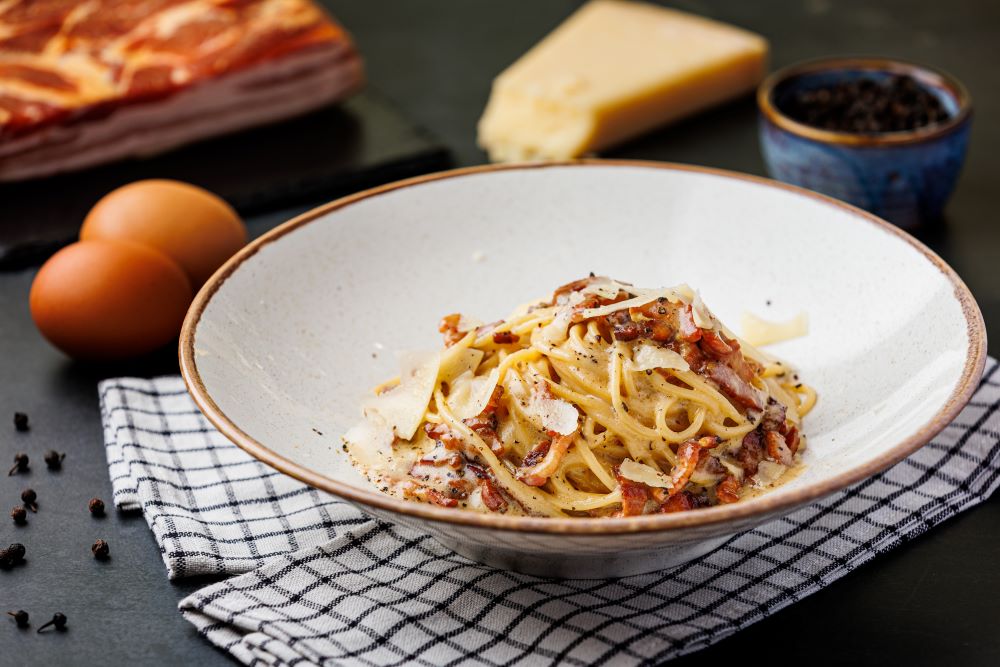 White plate with spagetthi, permesan and bacon pieces