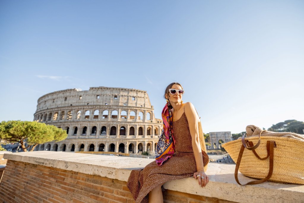 A young woman sitting on a wall with the Colosseum of Rome in the background.