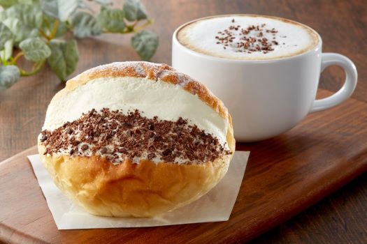 A roll filled with cream and cocoa powder and a cup of cappuccino