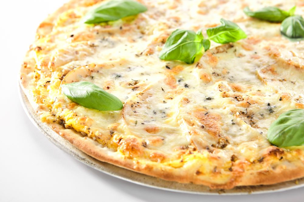A pizza with creamy white sauce, cheese and garnished with basil