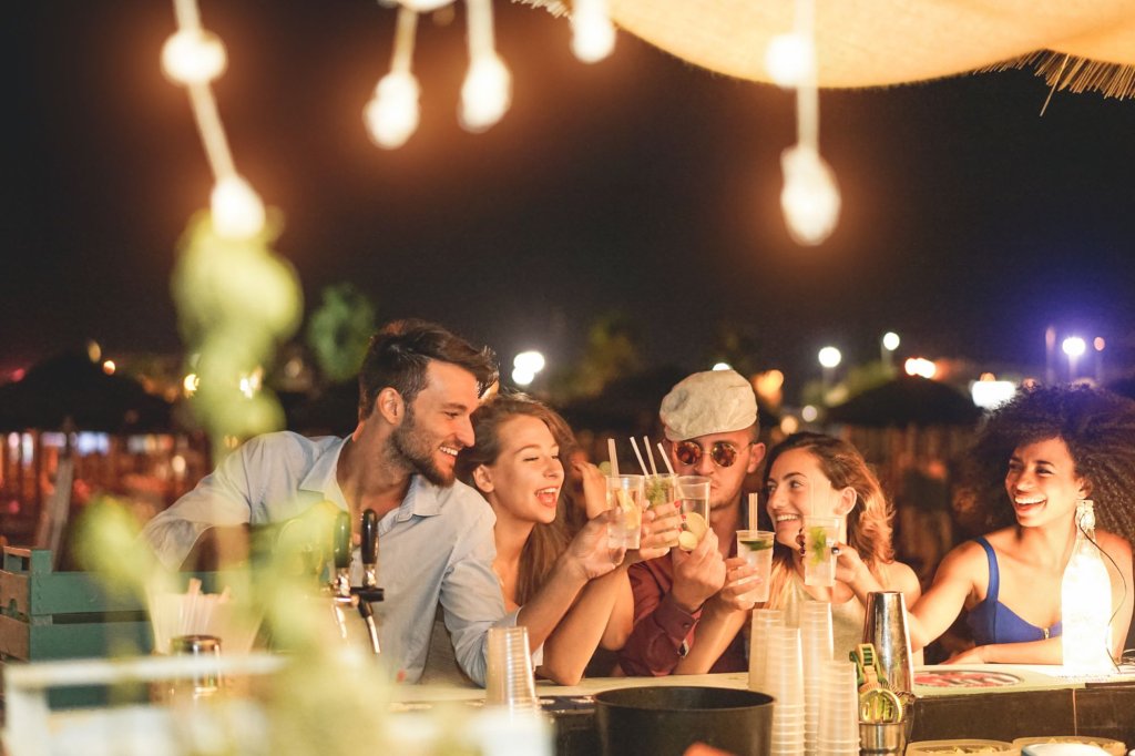 A group of young people on a rooftop terrace having a drink together during the night.