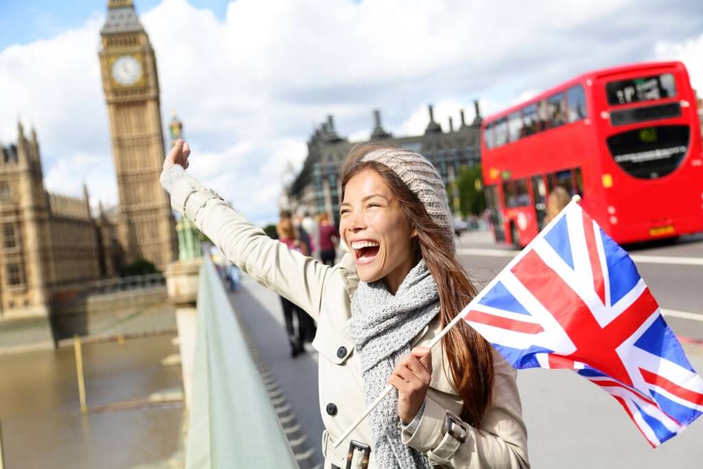 A laughing woman on a bridge in London with a UK flag