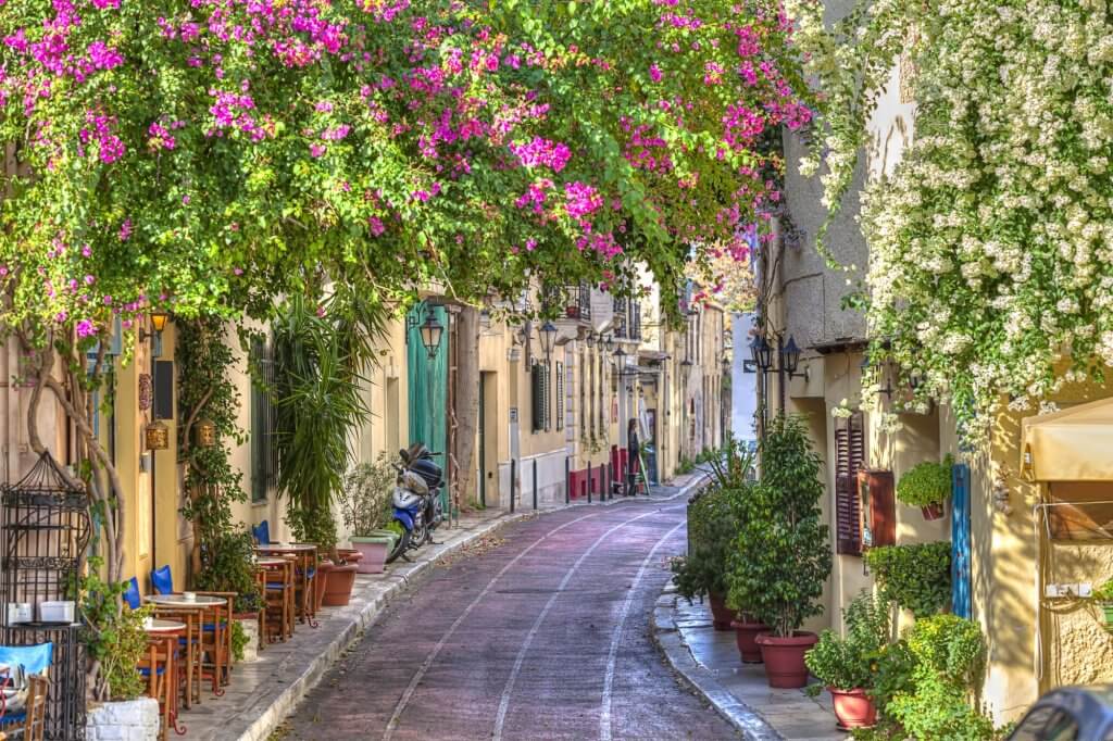 View of a small alley with lots of pink flowers and green houses in Athens.