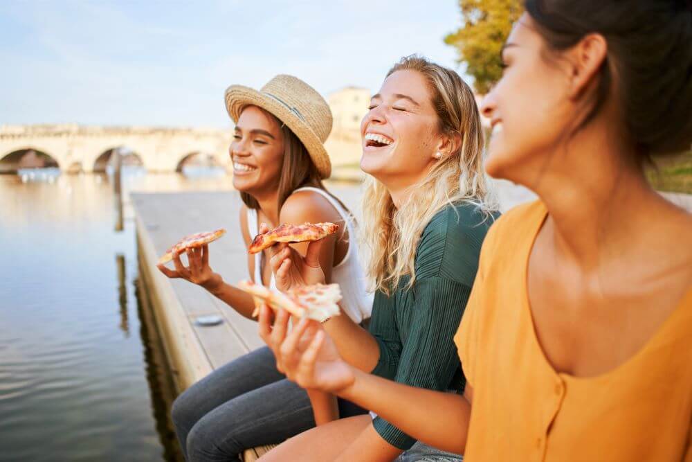 Three beautiful women eating pizza outdoors.